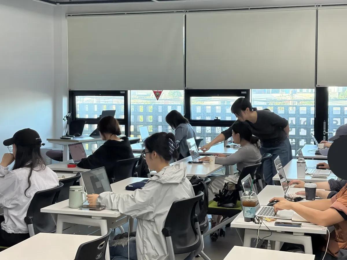 강사가 수강생 옆에서 노트북 화면을 가리키며 설명하는 장면